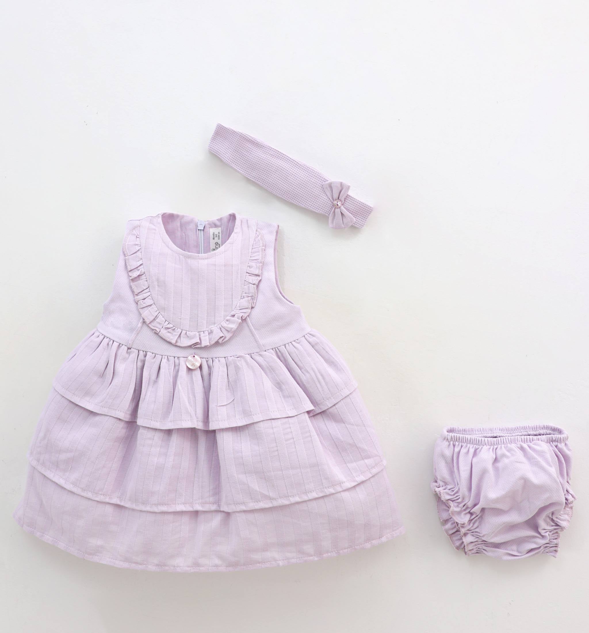 Lavender baby dress with ruffles, matching headband, and bloomers on a white background.