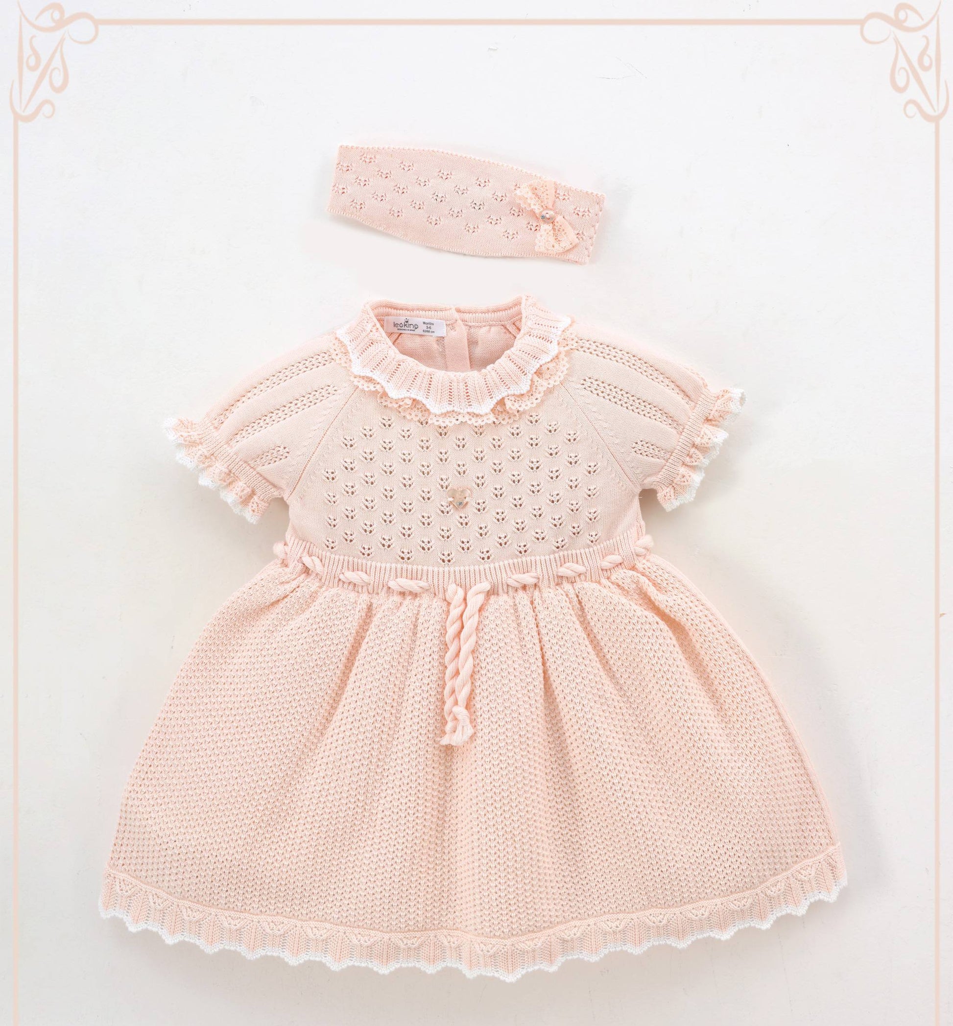 Pink baby dress with ruffled collar and matching headband on a light background