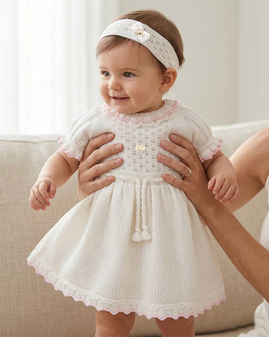 Baby in a white lace dress held by an adult, sitting on a couch.