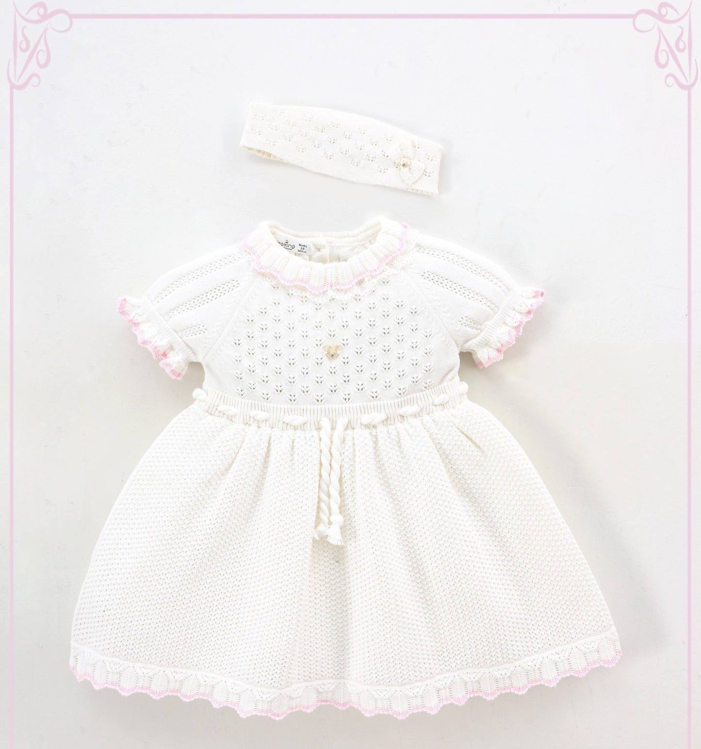 White baby dress with pink trim and matching headband on a light pink background