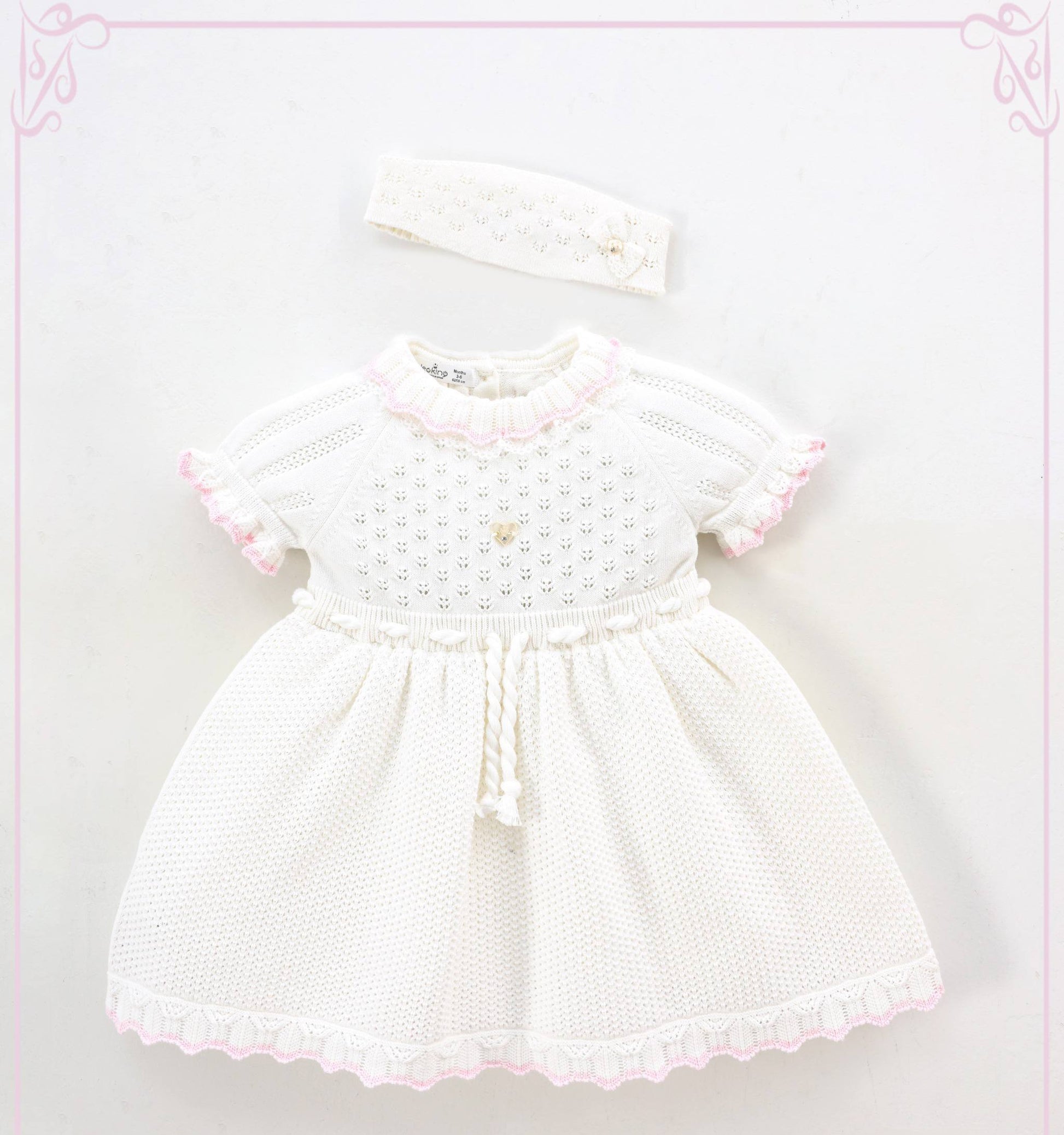White baby dress with pink trim and matching headband on a light pink background