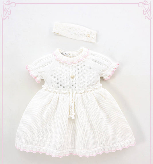 White baby dress with pink trim and matching headband on a light pink background