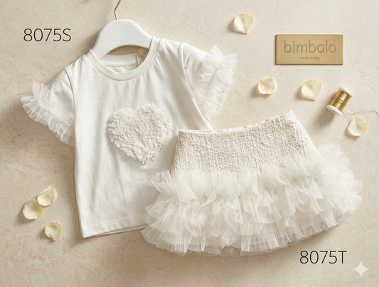 A baby girl's two-piece outfit set featuring a white short-sleeve top with ruffle trim and a textured heart applique, paired with a white ruffled tutu skirt. The set is styled on a beige textured background with decorative rose petals, a gold spool of thread, and a gold brand tag reading 'bimbaló made in Italy'.